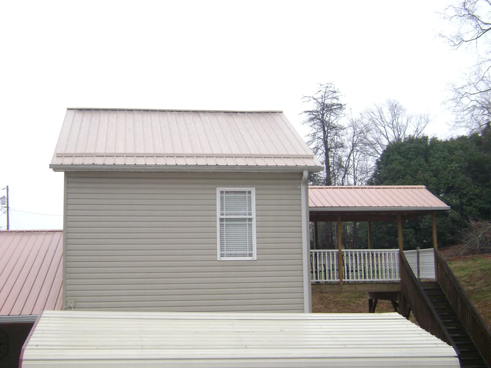 Tan metal roofs on a two story addition and attached porch, from a Roof Replacement job in Rawlings